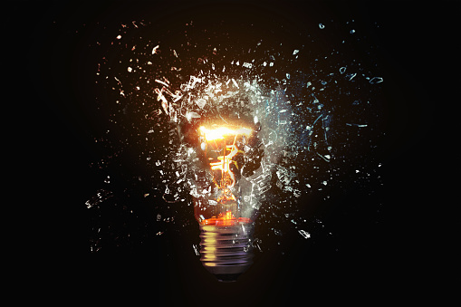 Creative idea light bulb explodes with shards of glass against a dark background. Business, ideas and new thinking, concept. Think Different. Go beyond what is possible.